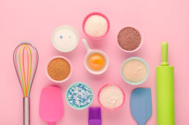 fırın malzemeleri, yumurta, un, kakao, şeker ve mutfak aletleri pembe arka planda