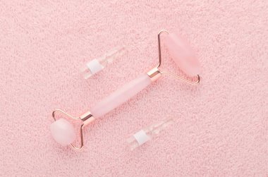 Gerçek gül kuvars yüz silindiri ve pembe arkaplandaki ampullerde yüz serumu