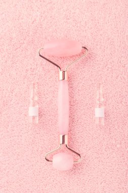 Gerçek gül kuvars yüz silindiri ve pembe arkaplandaki ampullerde yüz serumu