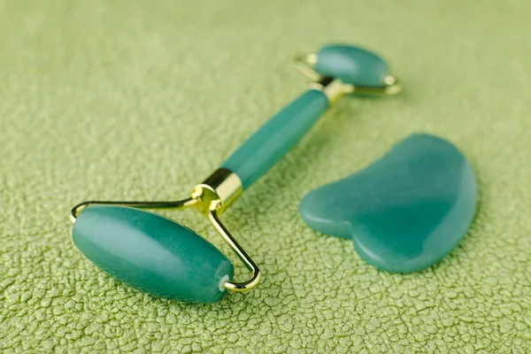 Real jade facial roller and massage stone gua sha on green background, closeup — Stock Photo, Image