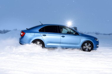 Vorkuta, Komi / Rusya - 12 01 2018: Kışın kar altında farları açık halde Skoda Rapid mavi araba. Kar fırtınasında dinamik hareket ve arabanın geri dönüşü.