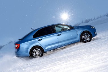 Vorkuta, Komi / Rusya - 12 01 2018: Kışın kar altında farları açık halde Skoda Rapid mavi araba. Kar fırtınasında dinamik hareket ve arabanın geri dönüşü.
