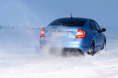 Vorkuta, Komi / Rusya - 12 01 2018: Kışın kar altında farları açık halde Skoda Rapid mavi araba. Kar fırtınasında dinamik hareket ve arabanın geri dönüşü.