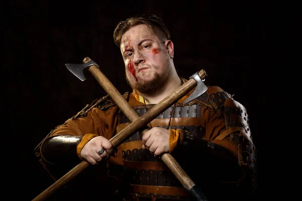 A Scandinavian warrior viking wounded in leather and metal armor with a fighting axe on a dark background. Blood and chopped wound