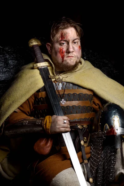 A Scandinavian warrior viking wounded in leather and metal armor with a fighting axe on a dark background. Blood and chopped wound