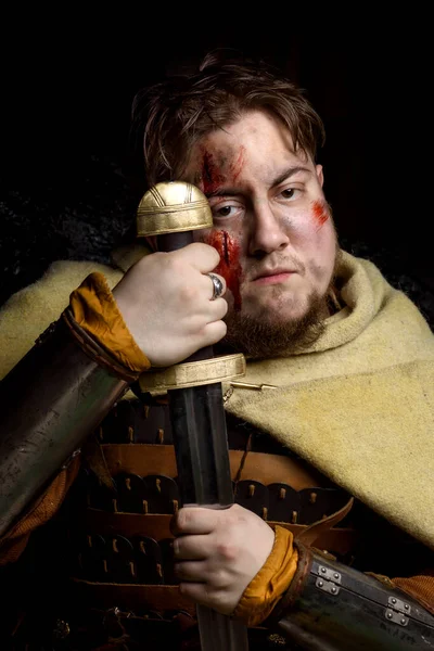 A Scandinavian warrior viking wounded in leather and metal armor with a fighting axe on a dark background. Blood and chopped wound