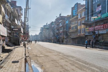 25 Mart 2020. Katmandu, Nepal. Boudha bölgesinde. Issız bir caddenin ve karantina altındaki dükkanların arka planında, uzaktaki tek polis ve yalnız pederlerin....