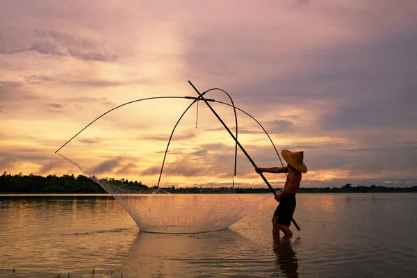 Pescatore all'alba silhouette con attrezzi da pesca sul lago — Foto Stock