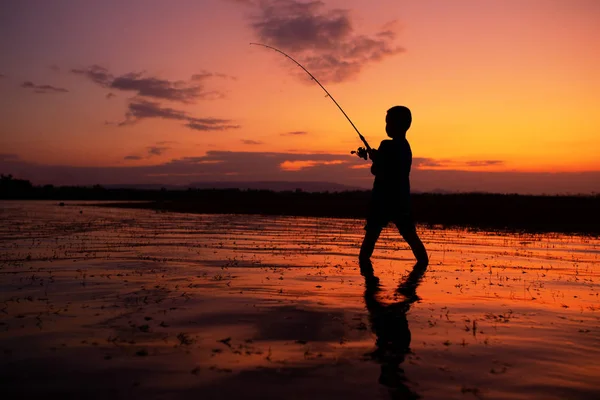Мальчик рыбачит на озере во время силуэта заката жизни — стоковое фото