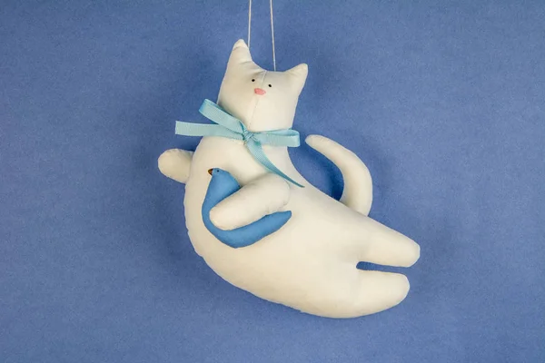Handmade white cotton cat toy flying on the blue sky with bird in hand paw / cute baby toys / kitty with simple bow-knot / close up background
