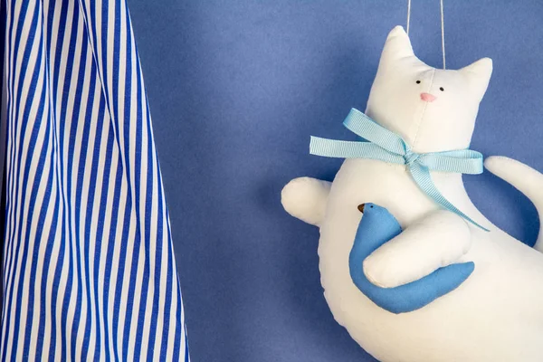 Handmade white cotton cat toy flying on the blue sky with bird in hand paw / cute baby toys / kitty with simple bow-knot / close up background