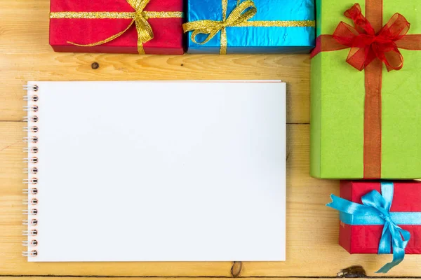 Presente cajas en el concepto de vacaciones de tarjetas de felicitación de fondo de madera. Navidad coloridas cajas de regalo en la mesa de madera. Vista superior con espacio de copia. Cuaderno de notas —  Fotos de Stock