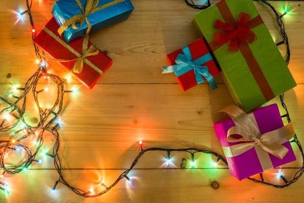 Presente cajas en el concepto de vacaciones de tarjetas de felicitación de fondo de madera. Navidad coloridas cajas de regalo en la mesa de madera. Vista superior con espacio de copia. Navidad romántica luces marco sobre fondo de madera . —  Fotos de Stock