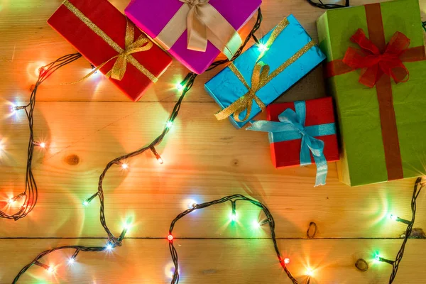 Presente cajas en el concepto de vacaciones de tarjetas de felicitación de fondo de madera. Navidad coloridas cajas de regalo en la mesa de madera. Vista superior con espacio de copia. Navidad romántica luces marco sobre fondo de madera . —  Fotos de Stock