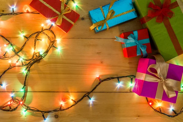 Presente cajas en el concepto de vacaciones de tarjetas de felicitación de fondo de madera. Navidad coloridas cajas de regalo en la mesa de madera. Vista superior con espacio de copia. Navidad romántica luces marco sobre fondo de madera . —  Fotos de Stock