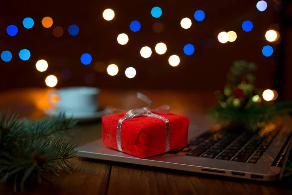 Laptop ve ahşap masa Noel ışıkları ile üzerine kırmızı hediye kutusu — Stok fotoğraf