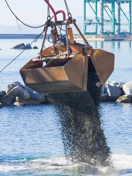 Dredge Clamshell Bucket unloading gravel in the water of a port Stock Picture