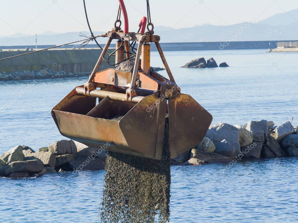 Dredge Clamshell Bucket unloading gravel in the water of a port