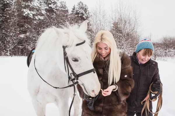 Girl, horse trainer and white horse on a winter