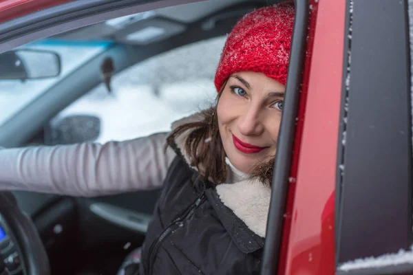 Girl in a red cap and warm jacket in a red car in a winter