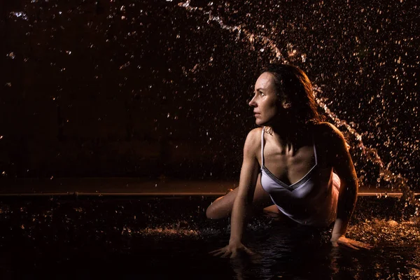 Girl in white dress in water in a dark water in pool in studio and dark background