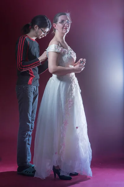 Young male assistant helps old actress to zip up white dress on stage with light of spotlight