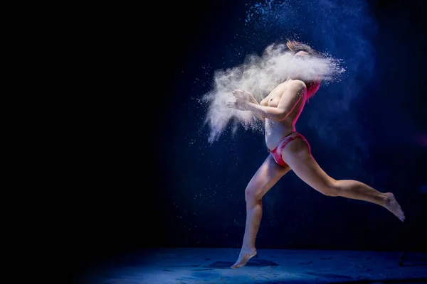 Old fat naced female dancer tries to dance in the studio during photoshoot with flour on a black background