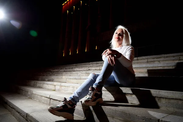 Ugly woman on the steps of stair in the city at night with light