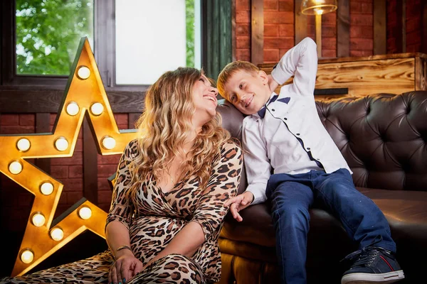 Beautiful elegant pregnant woman with blonde curly hair with small boy in the room. Mother having fun with young son in living room. Maternity concept