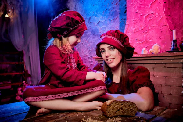 Easter and family. Mother and daughter in maroon or red dresses of village shepherdesses and small chicken in rural wooden interior in studio. Colour beautiful light background of two female relatives