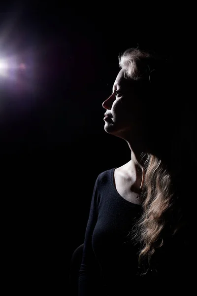 Portrait of a girl illuminated by the contour light of a flash on a black dsrk background