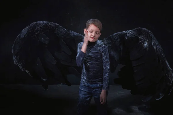 Black evil angel on a dark background with colored lighting. The concept of war between good and evil. Boy with angel wings during a photoshoot with flour and loose powder