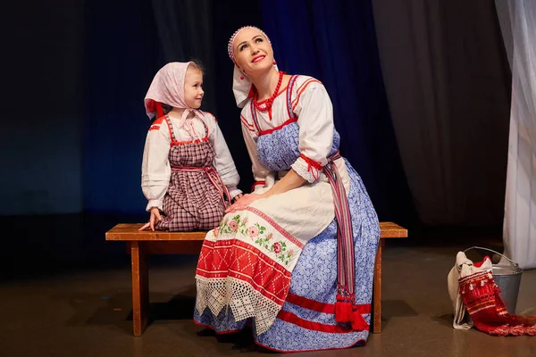 Little girl and an adult woman in Russian national dress posing during photoshoot on stage. Mother and daughter together