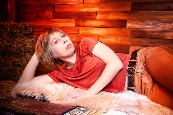 Ugly pity Girl in red dress on the couch with hay in the room or in the hayloft with wooden walls. Rustic style in the interior during photoshoot