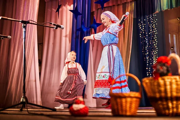 Little girl and adult woman in Russian national dress rehearsing on stage. Mother and daughter sing and dance together