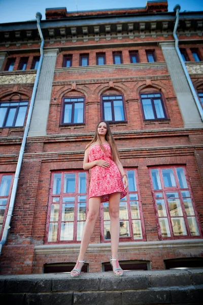 Brunette girl near red brick facade of old building in the central part of city in a summer day. Portrait of pretty girl on the street of town. Walk in downtown