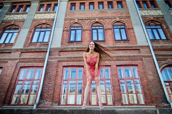 Brunette girl near red brick facade of old building in the central part of city in a summer day. Portrait of pretty girl on the street of town. Walk in downtown