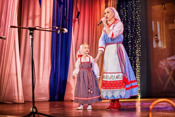 Little girl and adult woman in Russian national dress rehearsing on stage. Mother and daughter sing and dance together