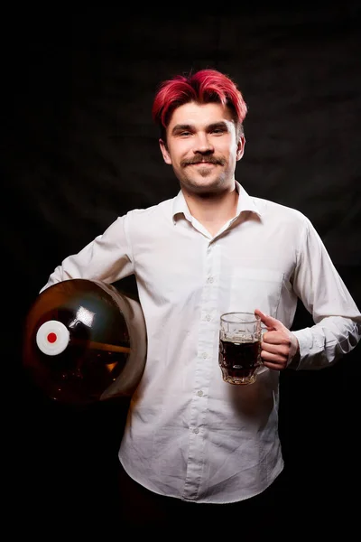 Young handsome guy with red hair in white shirt with beer. Funny man with large bottle of beer and black background. Brewer and barrel. Happy alcoholic with alcohol