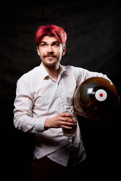 Young handsome guy with red hair in white shirt with beer. Funny man with large bottle of beer and black background. Brewer and barrel. Happy alcoholic with alcohol