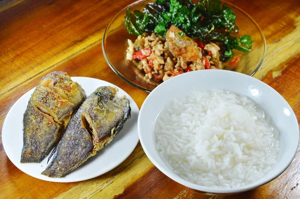 Boiled rice eat with stir fried crispy basil leaf with black preserved egg and deep fried fish — Stock Photo, Image