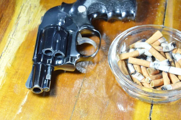Περίστροφο πιστόλι και το τσιγάρο στο τασάκι με γυαλί στο ξύλινο τραπέζι — Φωτογραφία Αρχείου