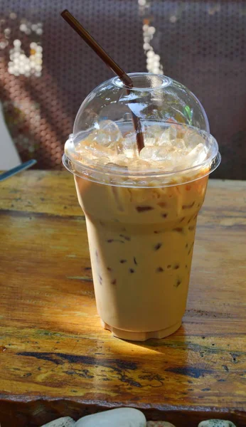 Eiskaffee in Plastikbecher auf Holztisch mit Morgensonne — Stockfoto