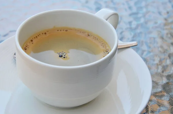 玻璃桌上的白色杯中的黑色浓缩咖啡 — 图库照片