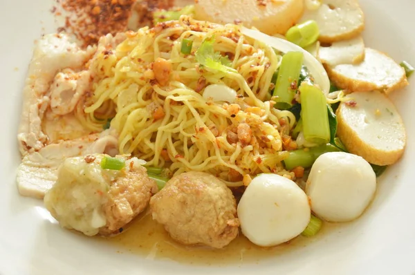 Mie kuning pedas Cina kering topping ikan dan bola udang dengan irisan daging babi rebus di piring — Stok Foto
