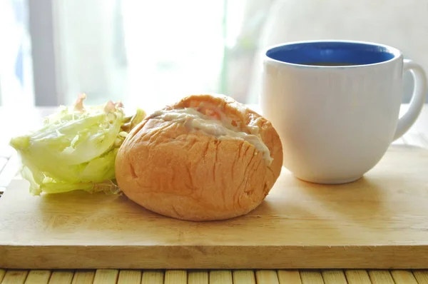 Bollo relleno de mayonesa de atún y lechuga con taza de café en bloque de chuleta de madera — Foto de Stock