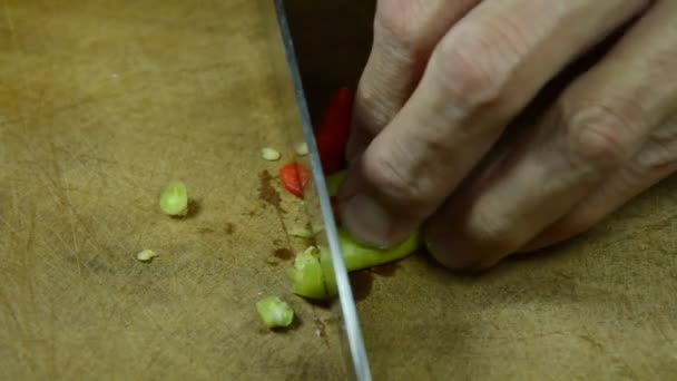 Hand snijden van rode en groene chili door keukenmes op houten hakken blok — Stockvideo