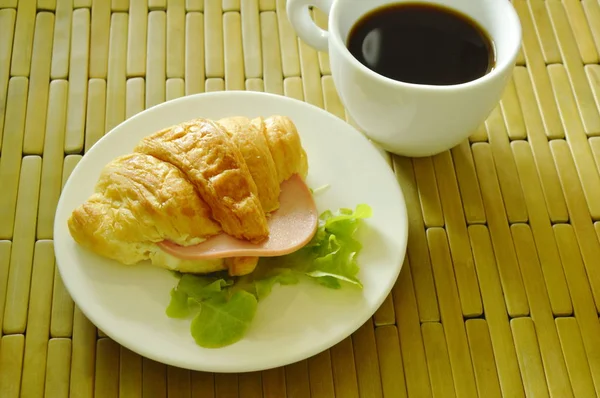 Croissant fyllda fläsk bologna och grön ek äta par med svart kaffe — Stockfoto