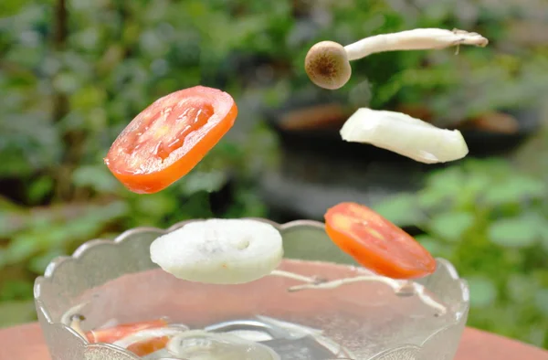 Pomodoro e cipolla con funghi che cadono in acqua sulla ciotola di vetro — Foto Stock