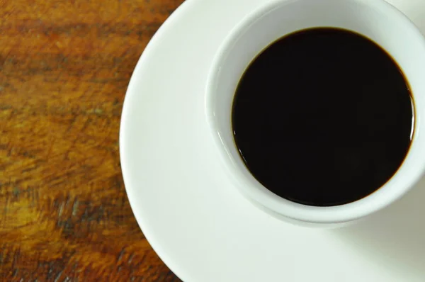 Taza de café caliente negro en plato sobre mesa de madera —  Fotos de Stock